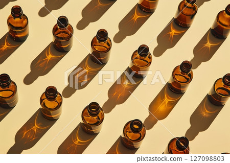 Amber glass dropper bottles are neatly arranged in a pattern, casting striking shadows on a light-colored surface and creating an artistic display 127098803
