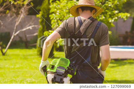 A man with a lawnmower cares for the grass in the backyard. 127099069