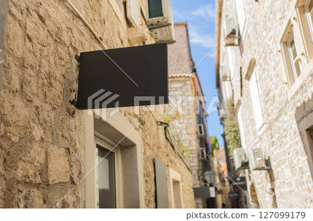 Blank signboard on stone building wall in Mediterranean alley. Concept of urban signage, empty brand space, and local European architecture. Copy space 127099179