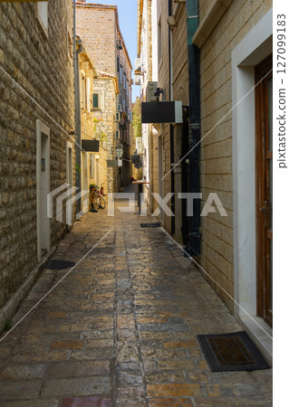 Narrow historic alley with stone buildings in Mediterranean old town. Cultural heritage, summer tourism, and urban charm 127099183