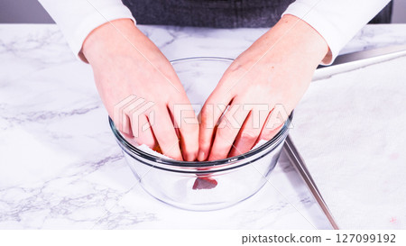 Strawberries, freshly washed and dried, are neatly stored in a glass bowl lined with a paper towel and securely covered with plastic wrap to maintain freshness. 127099192