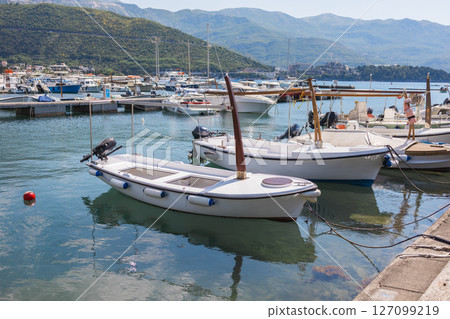 Small boats floating in marina with mountain backdrop. Coastal lifestyle, nautical tourism, and scenic summer destination. 127099219
