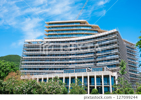 Modern glass building under construction with full scaffolding. Urban development, contemporary architecture, and city infrastructure progress. Modern glass building under construction with full scaffolding. Urban development, contemporary architecture, and city infrastructure progress. 127099244