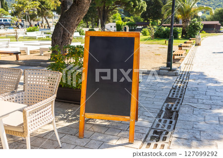 Wooden frame chalkboard stands on summer pavement. The concept shows outdoor signage, seasonal business, and blank advertising opportunity. Copy space. 127099292