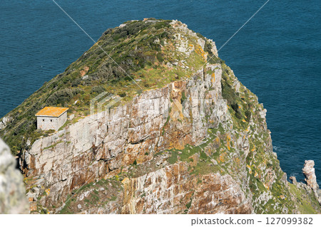A cliff surrounded by the ocean and a house on the edge of rocky cliff 127099382