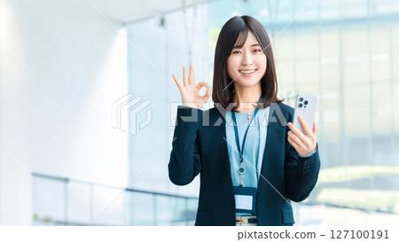 一位微笑的女人/女商人拿著智慧型手機，做出「OK」的姿勢 127100191