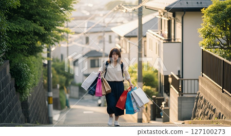 A woman climbing a hill carrying a lot of luggage 127100273