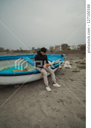 Man Reads A Book In Solitude By The Sea On A Gloomy Day Man Reads A Book In Solitude By The Sea On A Gloomy Day 127100386