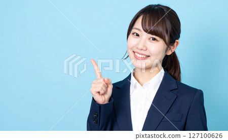 A young woman in a suit pointing and explaining with a bright smile 127100626