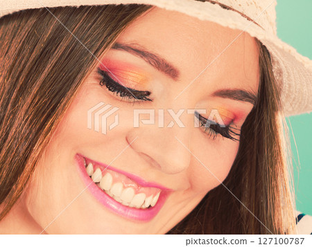 Woman face colorful eyes makeup, summer straw hat smiling Woman face colorful eyes makeup, summer straw hat smiling 127100787
