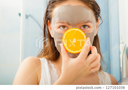 Woman with mud facial mask holds orange slice Woman with mud facial mask holds orange slice 127101036