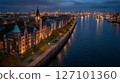 Port area illuminated at night, showcasing vibrant atmosphere with active vessels and stunning architecture along waterfront. Aerial view captures tranquil waters reflecting city lights. 127101360