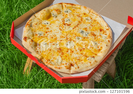 Cheese pizza in a red box on a stool on the grass. Food delivery, pizza. 127101596