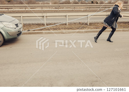 Woman pulling broken car on road Woman pulling broken car on road 127101661