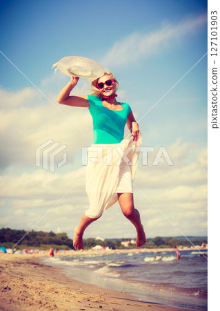Blonde woman wearing dress playing jumping on beach Blonde woman wearing dress playing jumping on beach 127101903