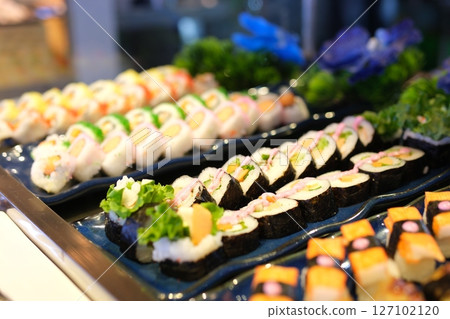 variety of colorful sushi rolls artfully arranged with cucumber slices and tuna sashimi 127102120