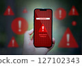 hand holding smartphone with red caution danger app icons 127102343