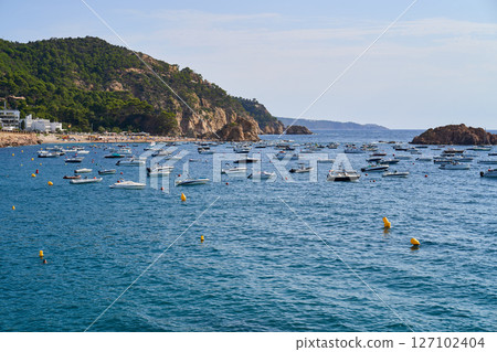 A scenic view of Tossa de Mar, showcasing boats floating in the sea with green hills and clear blue water under a bright sky. A scenic view of Tossa de Mar, showcasing boats floating in the sea with green hills and clear blue water under a bright sky. 127102404