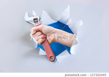 Hand with wrench emerging through wall. 127102445