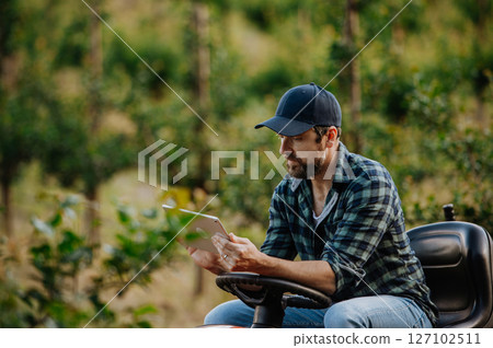 Farmer using digital tablet to inspect fruit trees in orchard. 127102511