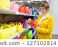 Portrait of elderly woman during shopping at mall. Red-haired elderly lady chooses a watering can at a home and garden goods store. 127102814