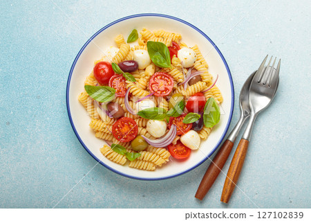Italian pasta salad with fusilli, cherry tomatoes, mozzarella, olives, basil on blue background top view, Italian cuisine Italian pasta salad with fusilli, cherry tomatoes, mozzarella, olives, basil on blue background top view, Italian cuisine 127102839