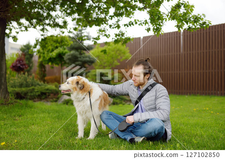 Young man owner walking with his large dog in public park on spring day. Pet care Young man owner walking with his large dog in public park on spring day. Pet care 127102850