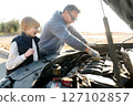 A middle-aged father and a preteen son work on a car during a road trip 127102857