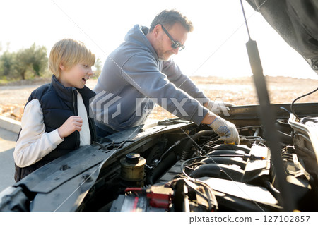 A middle-aged father and a preteen son work on a car during a road trip A middle-aged father and a preteen son work on a car during a road trip 127102857