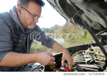 A middle-aged man repairs a car during a trip A middle-aged man repairs a car during a trip 127102859