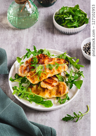 Crispy fried halloumi cheese and arugula leaves on a plate on a table vertical view 127102953