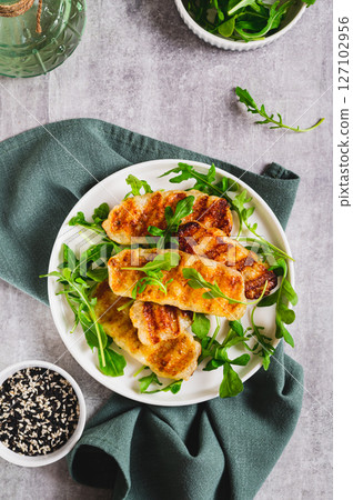 Crispy fried halloumi cheese and arugula leaves on a plate on a table top and vertical view 127102956