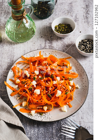 Homemade carrot slices in spices with ricotta and pumpkin seeds on a plate vertical view 127102962