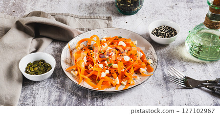 Spicy carrot, ricotta and pumpkin seed salad on a plate on a table web banner 127102967