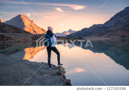 Young woman hiker with backpack standing near mountain lake 127103586