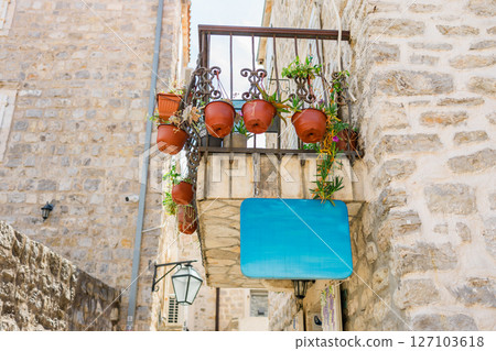Small balcony with flower pots and blank blue sign on stone building copy space. Mediterranean charm, outdoor decor and vintage architecture. 127103618