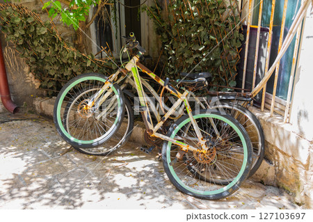 Two old vintage bicycles leaning against wall in shaded alley. Urban decay, nostalgic transport, and rustic Mediterranean charm. Two old vintage bicycles leaning against wall in shaded alley. Urban decay, nostalgic transport, and rustic Mediterranean charm. 127103697