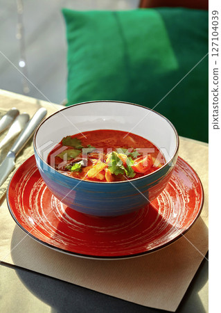 Tom yum soup served in blue bowl on red plate with cutlery aside 127104039