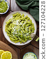 Top view of a plate of fusilli pasta with green pesto sauce and grated cheese on a wooden table 127104228