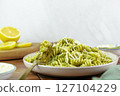 Plate of fusilli pasta with green pesto sauce and grated cheese on a wooden table 127104229