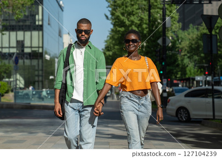 Pleased loving african american couple smiling walks in downtown together holding hands enjoy stroll 127104239