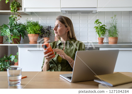 Pensive freelance woman procrastinating from laptop job at home, sit with smartphone, look at window 127104284