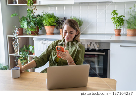 Smiling pleased woman freelance working procrastinating take break, surfing web in mobile phone. 127104287