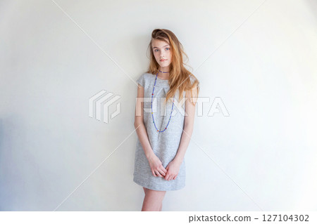 Happy teenage girl smiling. Closeup portrait young happy positive woman in grey dress at home in bright room against white wall. European woman. Positive human emotion facial expression body language 127104302