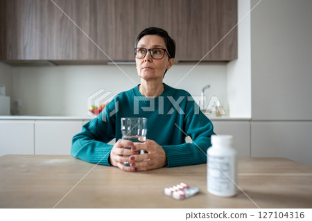 Sad woman swallows pills with water at home showing no emotion. Emotionless female consumes medicine Sad woman swallows pills with water at home showing no emotion. Emotionless female consumes medicine 127104316