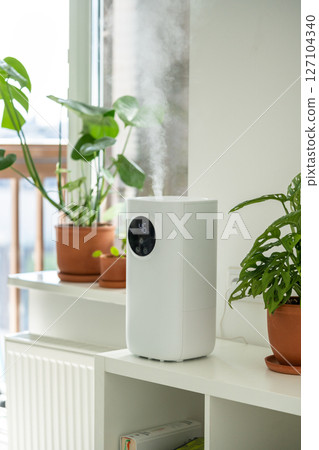 Modern humidifier at home, moistens dry air surrounded by indoor plant. Humidification concept Modern humidifier at home, moistens dry air surrounded by indoor plant. Humidification concept 127104340