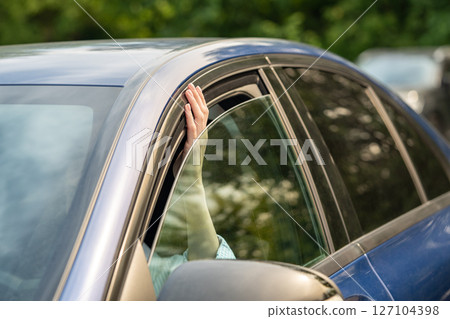 Woman checking hot weather temperature by sticking fingers out of slightly opened car window. Woman checking hot weather temperature by sticking fingers out of slightly opened car window. 127104398