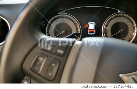 Car dashboard with illuminated open door icon behind defocused steering wheel 127104423