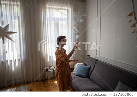Woman holding fragrant palo santo stick, using smoke for meditation and aromatherapy at cozy home.  127105003