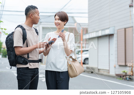 一名女子使用智慧型手機翻譯應用程式向外國人指路 127105908